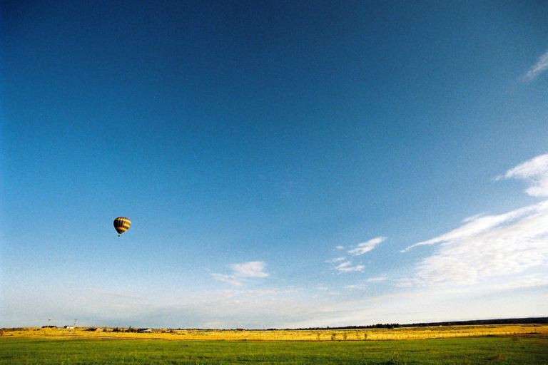 A hot air balloon floating in a vast blue sky above an open grassy field in Grand Teton National Park.