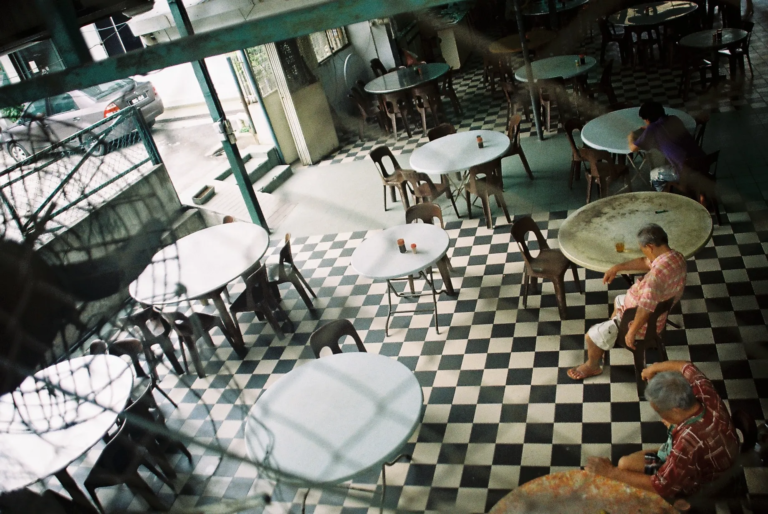 overhead view of an empty local restaurant with round tables and black-and-white tiled floor, two elderly men resting during the afternoon break, film photography by Percy Lin 2016