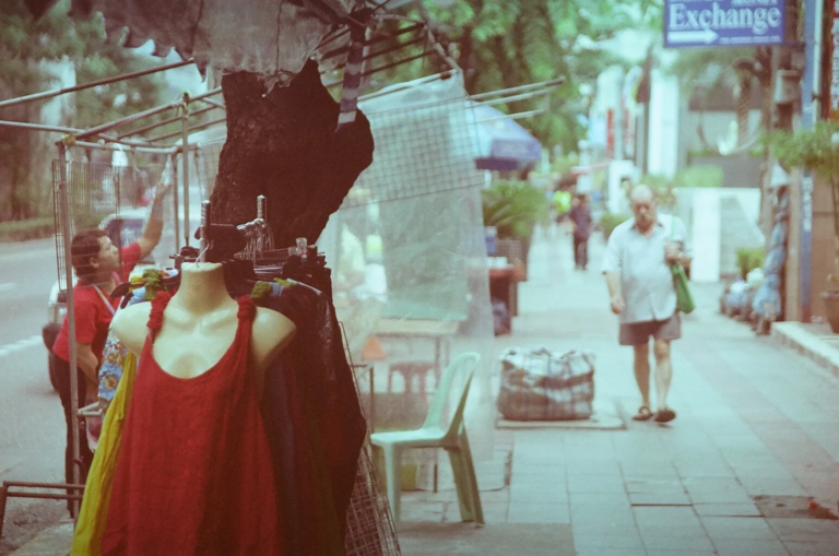 Street scene with a headless mannequin wearing a red dress and an elderly man walking away on a sidewalk in Bangkok, expired film tones, film photography by Percy Lin 2014