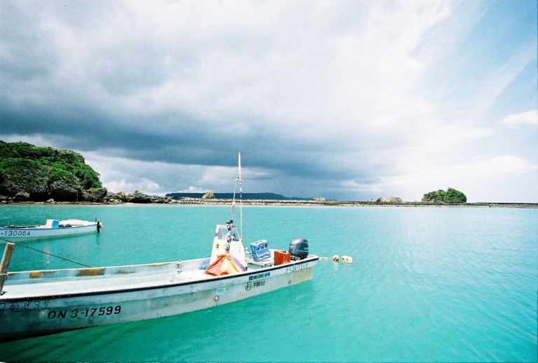 Turquoise harbor water with a small fishing boat under wide summer sky in Okinawa, film photography by Percy Lin 2016